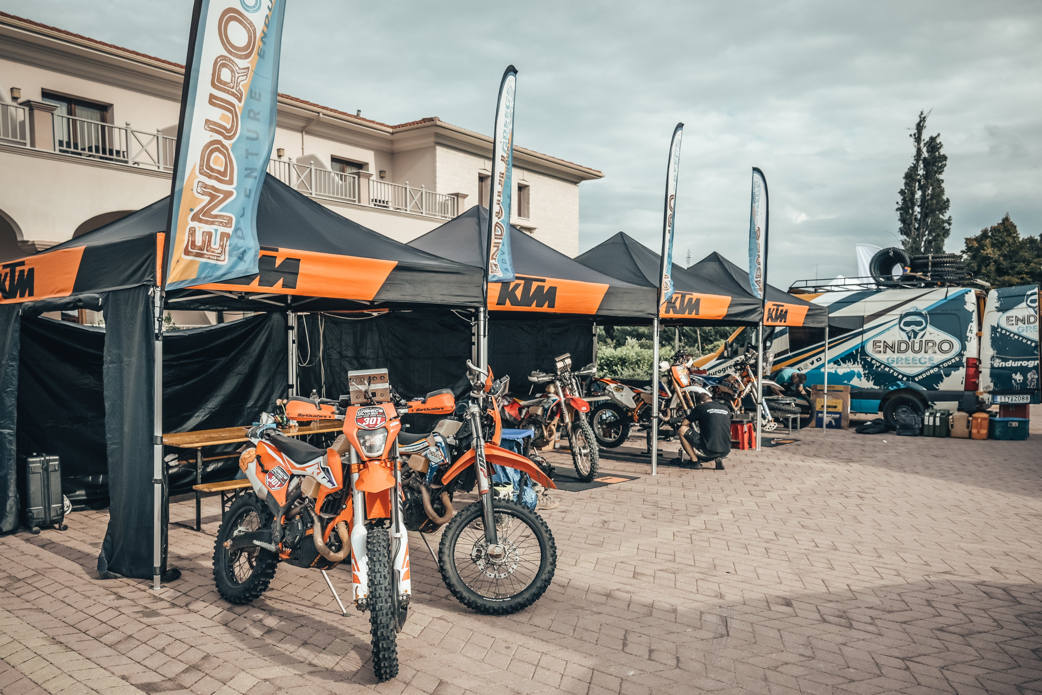 KTM rally bikes under branded tents with the Enduro Greece truck in the background